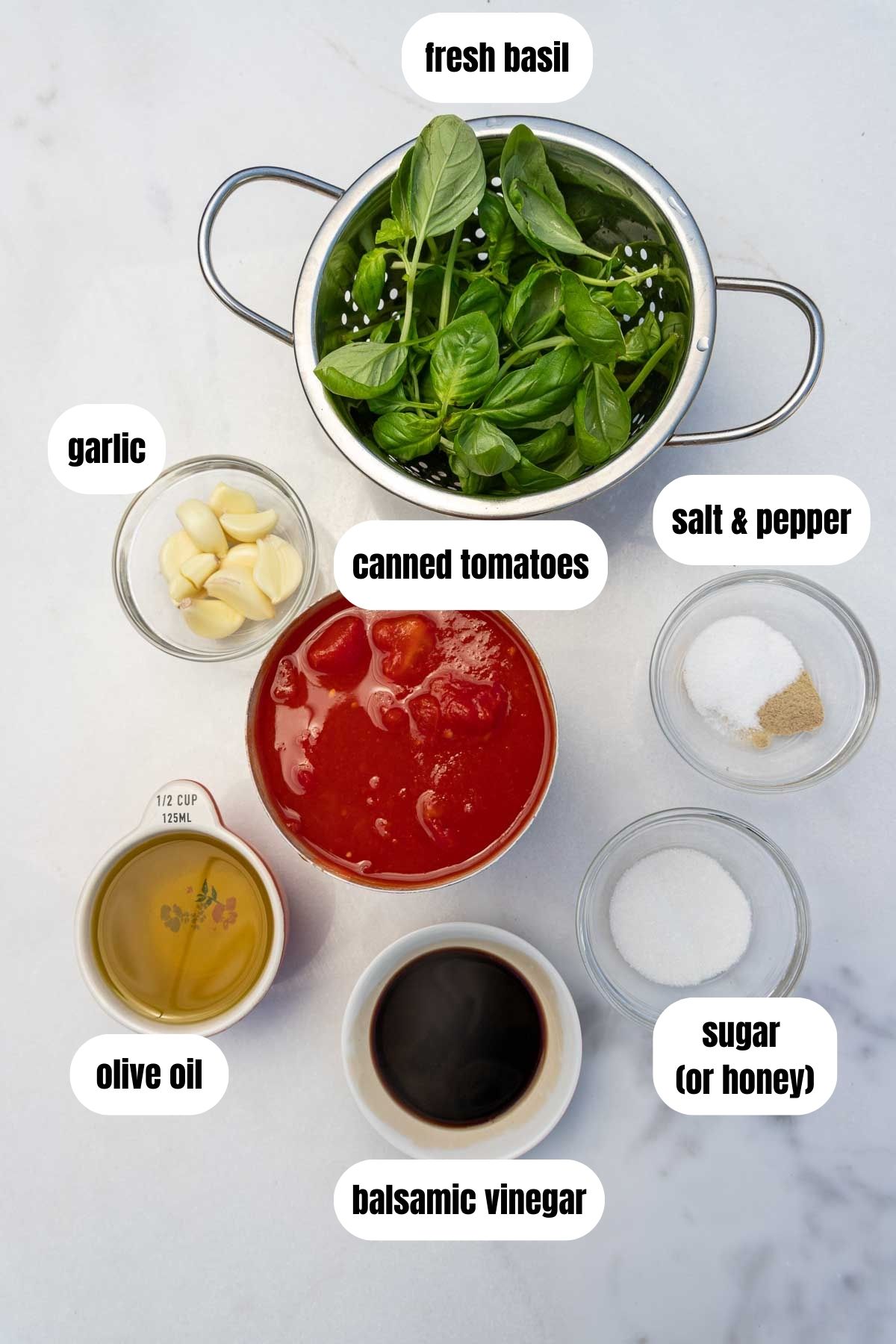 All ingredients for marinara sauce labelled including canned tomatoes, fresh basil, olive oil, balsamic vinegar, garlic, sugar or honey and salt and pepper.