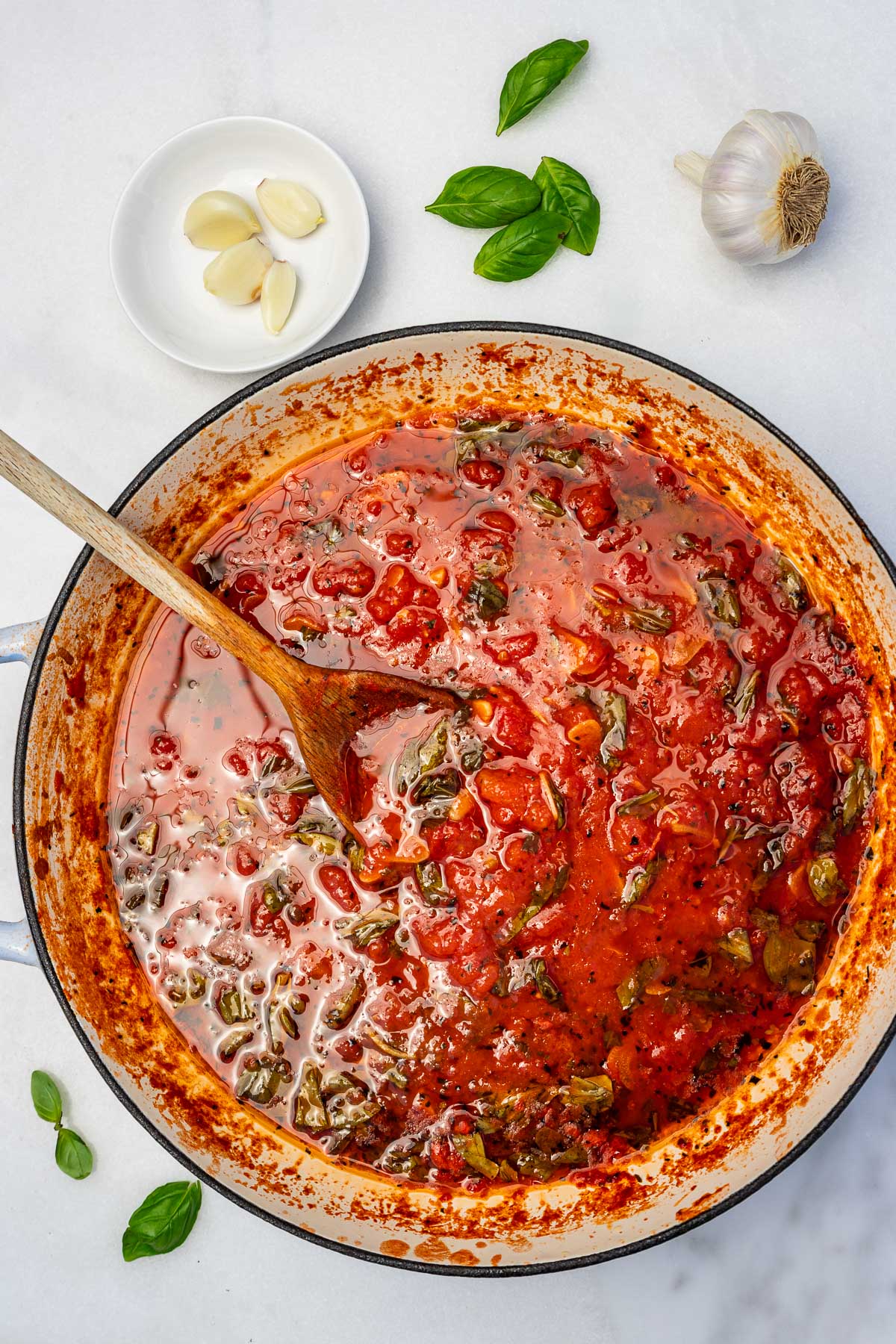 The top of a pan of homemade Italian marinara sauce with basil and a wooden spoon.