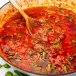 Closeup of a pan of homemade Italian marinara sauce with wooden spoon.