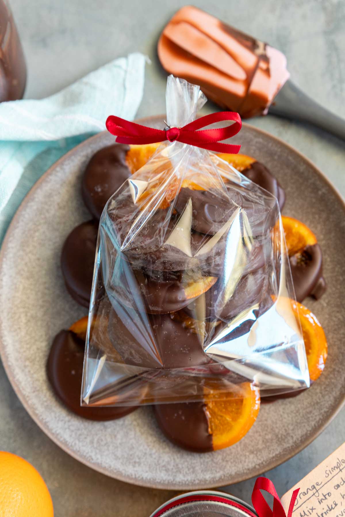 A small see-through gift bag with candied oranges dipped in chocolate in it, on a blue plate of more orange slices.