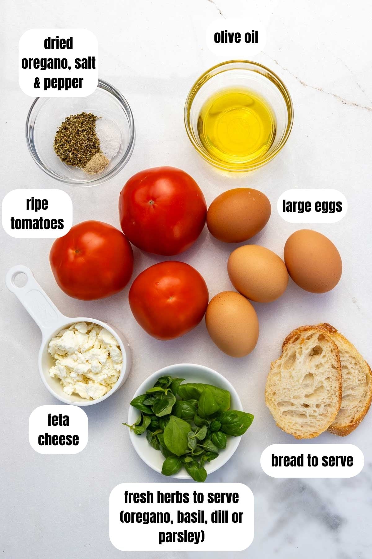 Labelled ingredients for Greek eggs including eggs, olive oil, tomatoes, feta cheese, oregano, salt and pepper and fresh herbs.