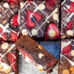 Closeup of the side of a strawberry white chocolate brownie with the rest of the pan of brownies slightly out of focus in the background.