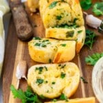 Air fryer garlic bread spread out on a wooden chopping board and with a wooden handled knife and ingredients at the side.