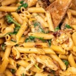 Closeup of the top of a pan of Marry Me Chicken Pasta with a wooden spoon in it.