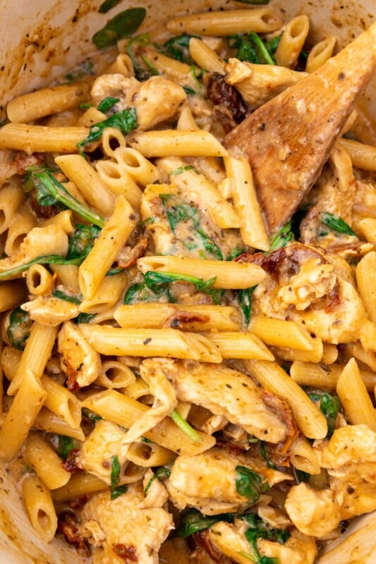 Closeup of the top of a pan of Marry Me Chicken Pasta with a wooden spoon in it.