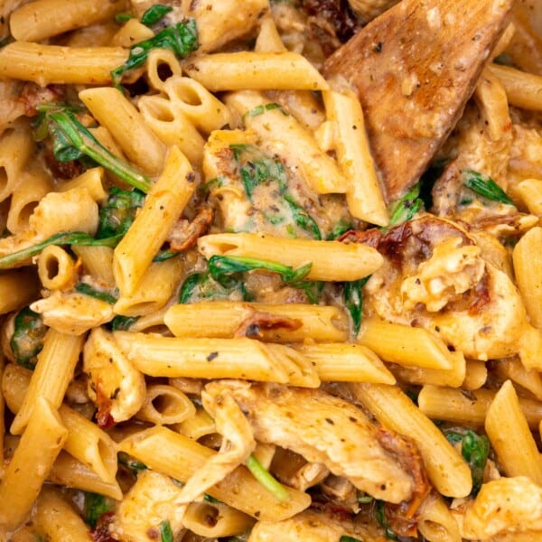Closeup of the top of a pan of Marry Me Chicken Pasta with a wooden spoon in it.