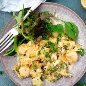 A blue plate of baked broccoli gnocchi with green salad and a fork, and with a pale blue tea towel at the top.