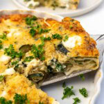Closeup of someone lifting a piece of crustless zucchini quiche out of a white quiche pan.