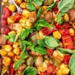 Closeup image of the top of a sausage and peppers sheet pan gnocchi dinner with lots of fresh basil on top.