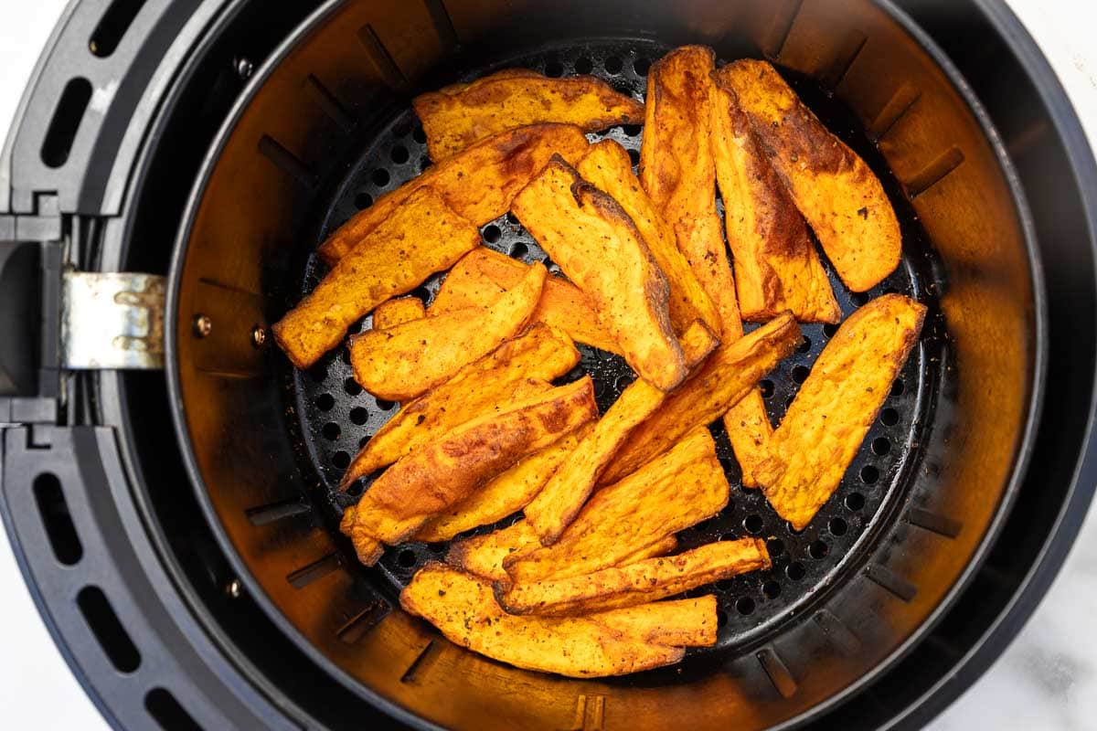 A closeup overhead view of crispy sweet potato wedges in a black air fryer basket.