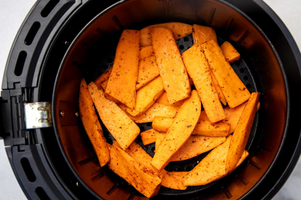 Overhead view of raw sweet potato wedges tossed in seasonings in the black basket of an air fryer.