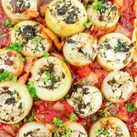 A pan of cooked Mediterranean style stuffed onions in a tomato sauce and with a decorative metal spoon in the pan.