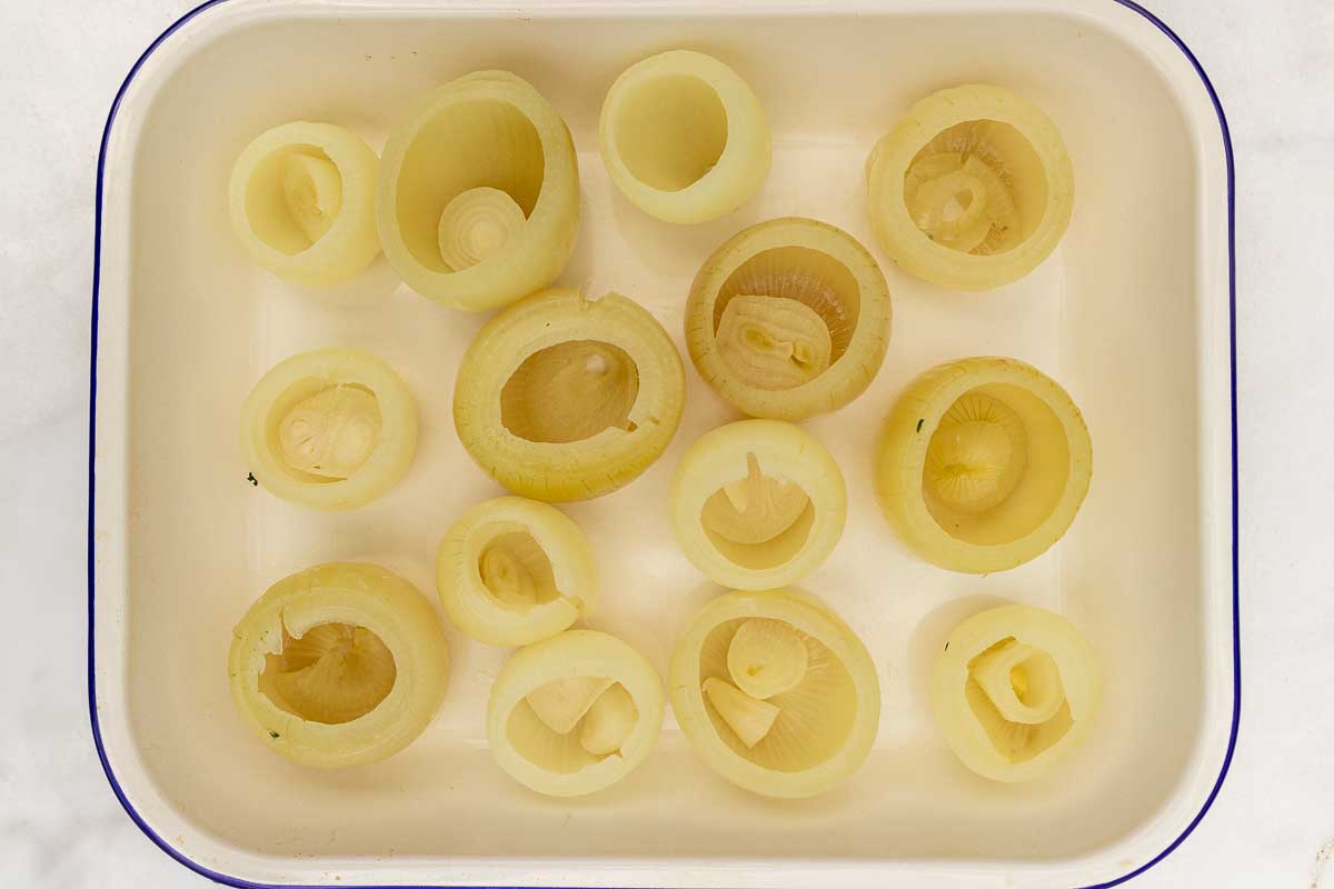 Par-boiled onions with the middles removed in a white pan with blue rim, ready to make stuffed onions.