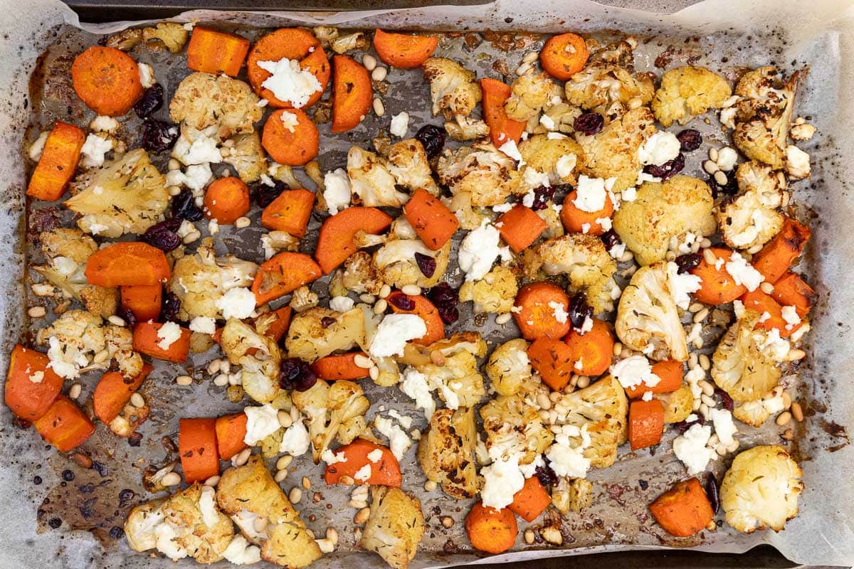 A lined baking sheet with roasted cauliflower and carrots scattered with feta, cranberries and pine nuts.