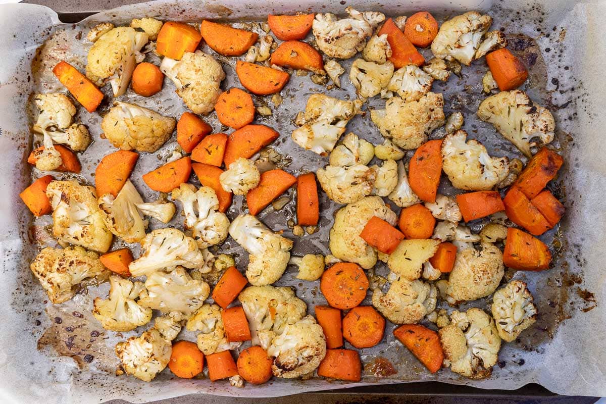 A lined baking sheet with cauliflower and carrots on it roasted with herbs and spices.