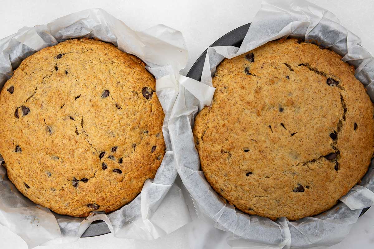 Two baked banana, peanut butter and chocolate chip cakes in lined baking pans, side by side.