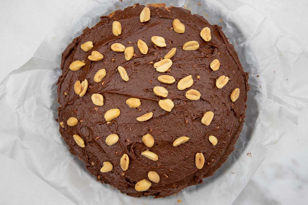 An overhead view of a peanut butter, banana and chocolate chip cake with chocolate frosting and peanuts on top.