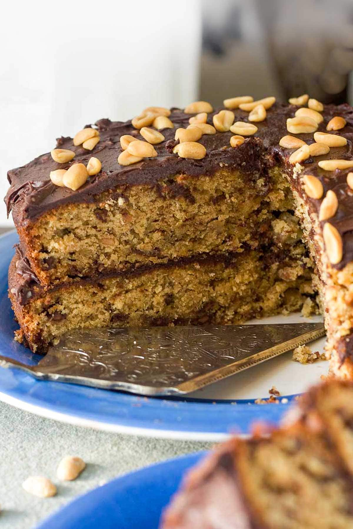 Closeup of the inside of a whole peanut butter banana chocolate layer cake with chocolate icing and peanuts on top on a blue plate with a decorative cake slice.