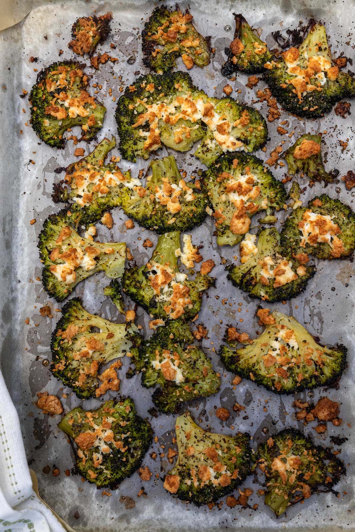 Overhead view of cooked smashed broccoli with browned feta on it on a baking pan lined with baking paper.