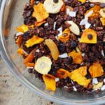 A closeup and overhead view of dark chocolate granola with dried fruit and nuts mixed in in a glass bowl.