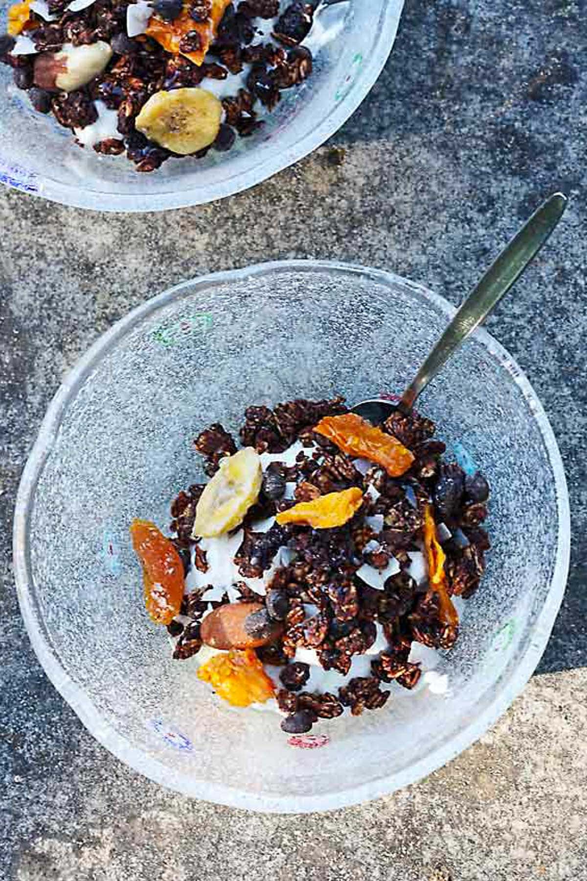 Overhead view of a bowl of homemade dark chocolate granola in a glass bowl, which another above it.