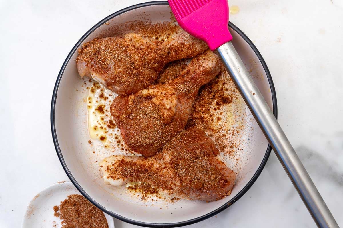 An overhead view of 3 raw seasoned chicken legs in a white bowl.