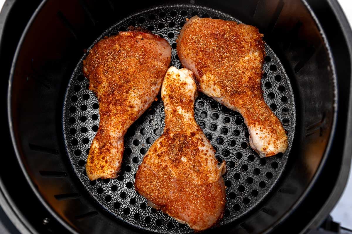 Overhead view of 3 seasoned chicken legs ready to be air fried in an air fryer basket.