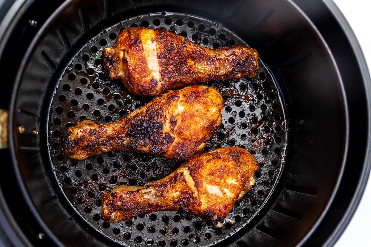 An overhead view of 3 BBQ seasoned chicken legs just cooked in an air fryer basket.