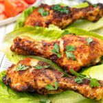 A closeup of 3 air fried chicken legs on a bed of lettuce and sprinkled with parsley.