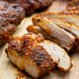 An air fried chicken thigh with golden seasoning on top and sliced on a wooden board.