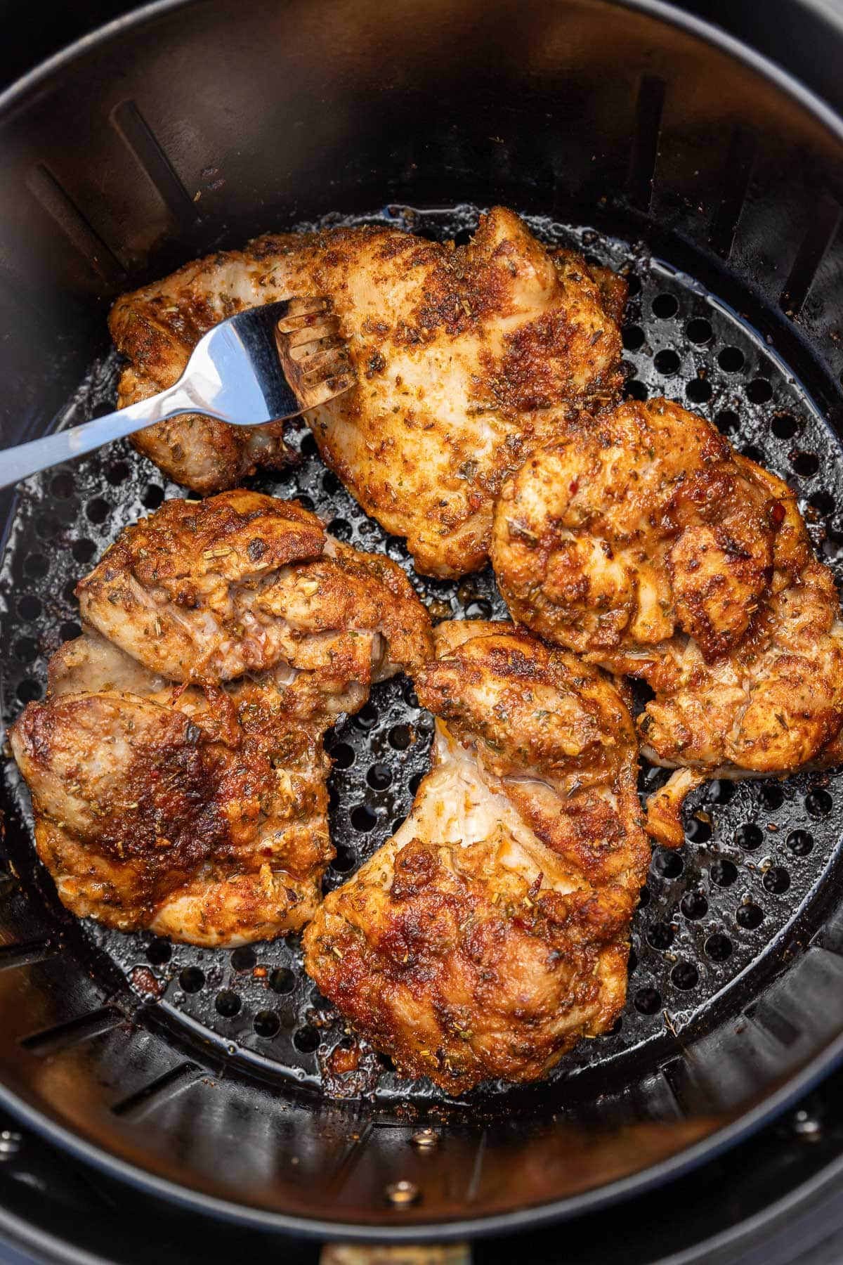 An overhead view of a closeup of 4 seasoned skinless boneless chicken thighs cooked in an air fryer basket.