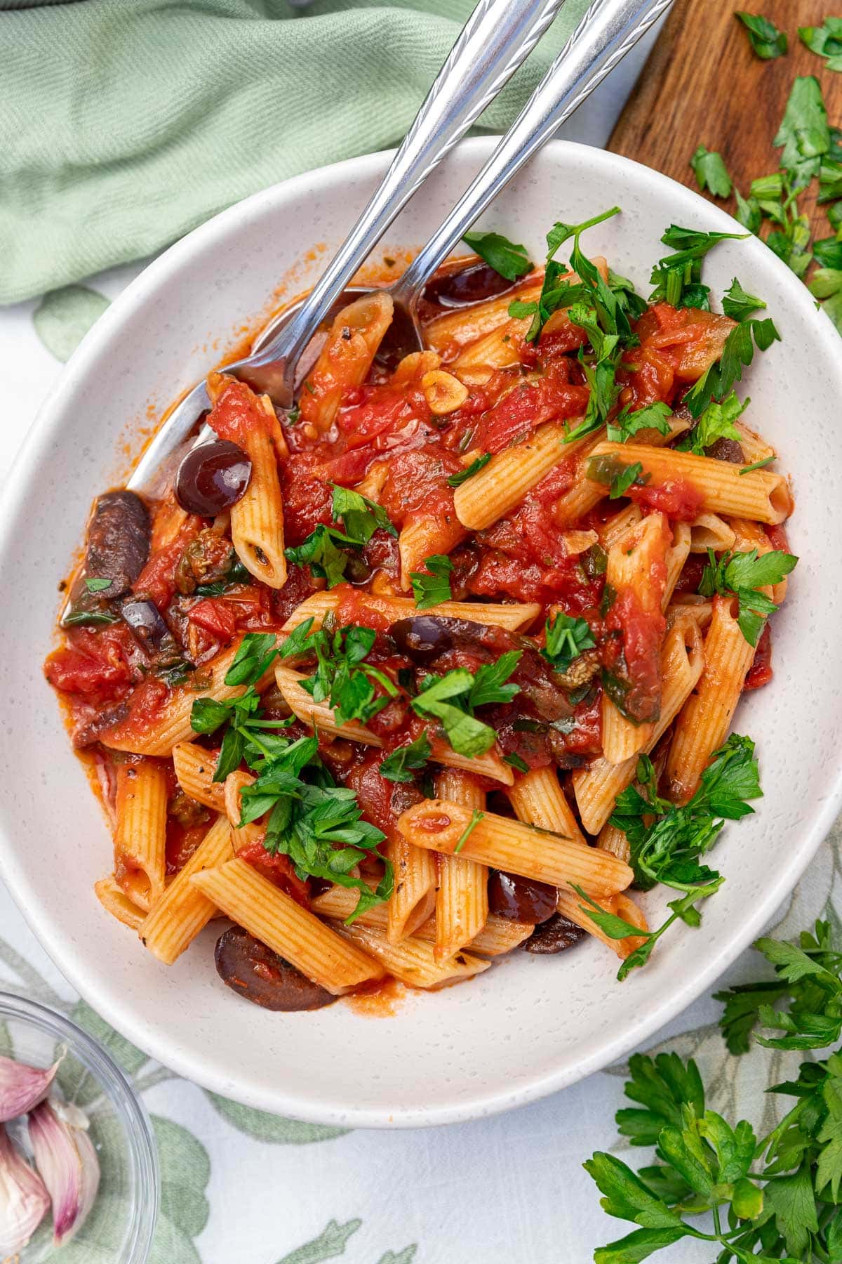 An overhead view of a white bowl of the pasta with fresh parsley on top and a spoon and fork in it.