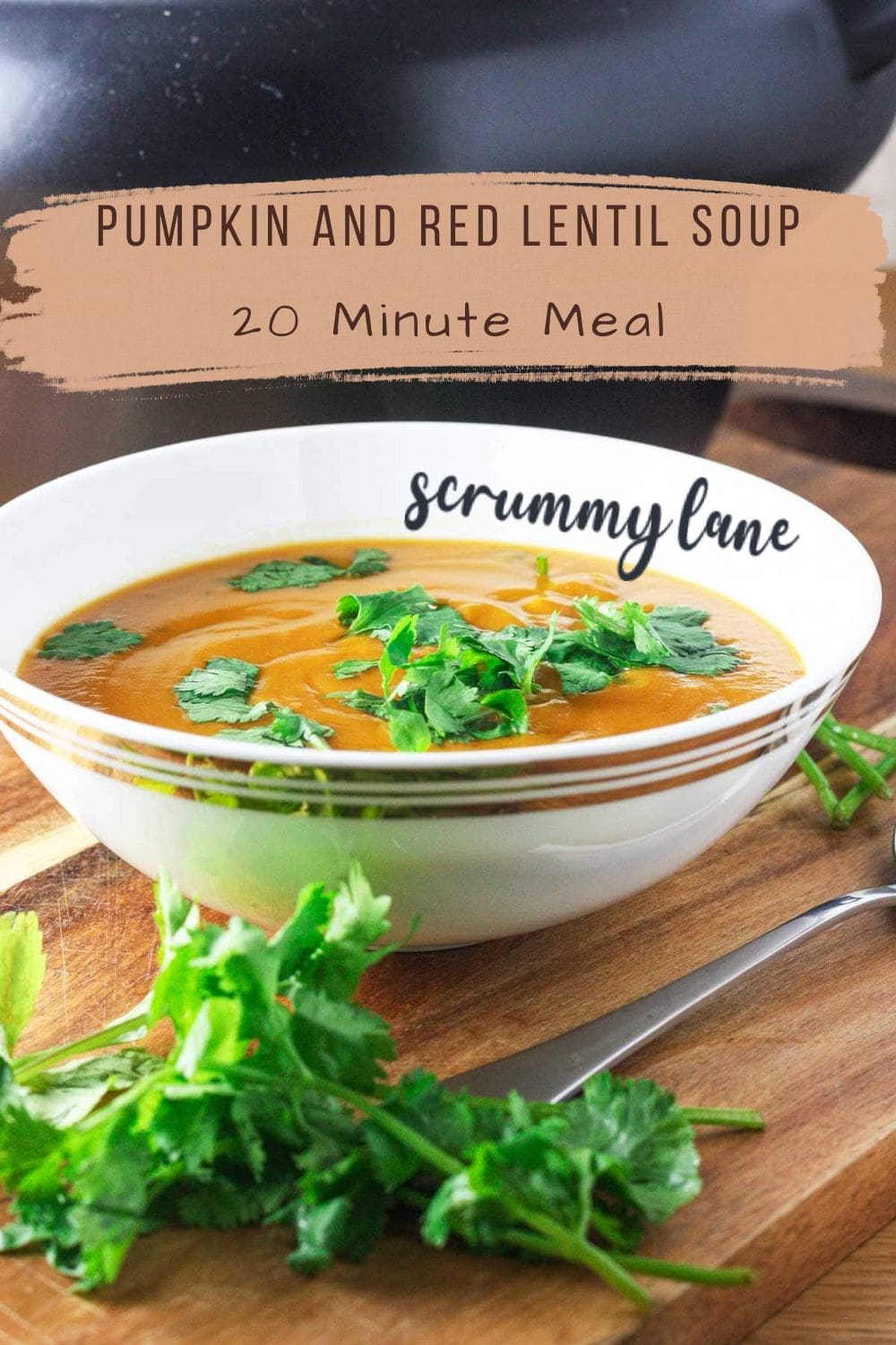 A white bowl of pumpkin and red lentil soup on a wooden board with herbs, with a title on it for Pinterest.