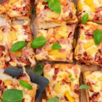 An overhead view of sheet pan Greek yogurt pizza sliced into rectangles, with fresh basil on top.