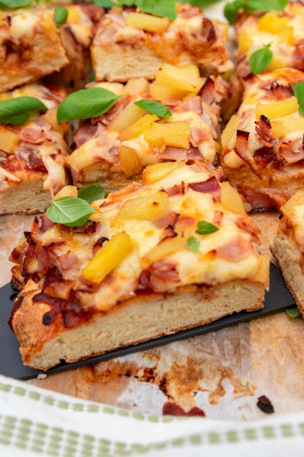 A closeup of a big slice of Greek yogurt pizza on a black pizza slice, with the rest of the pizza in the background.