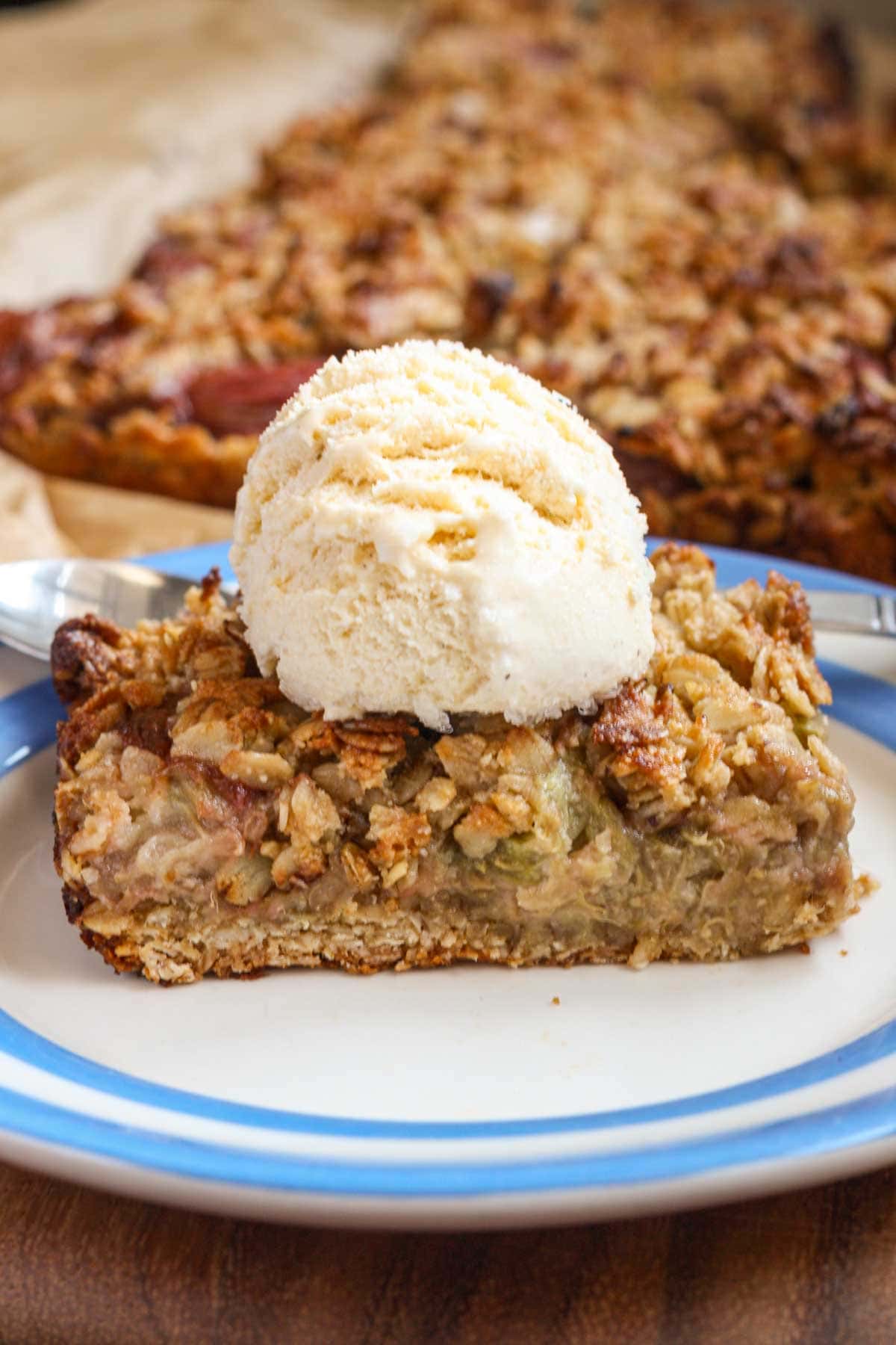 A rhubarb bar on a blue-rimmed plate with a scoop of vanilla ice cream on top.