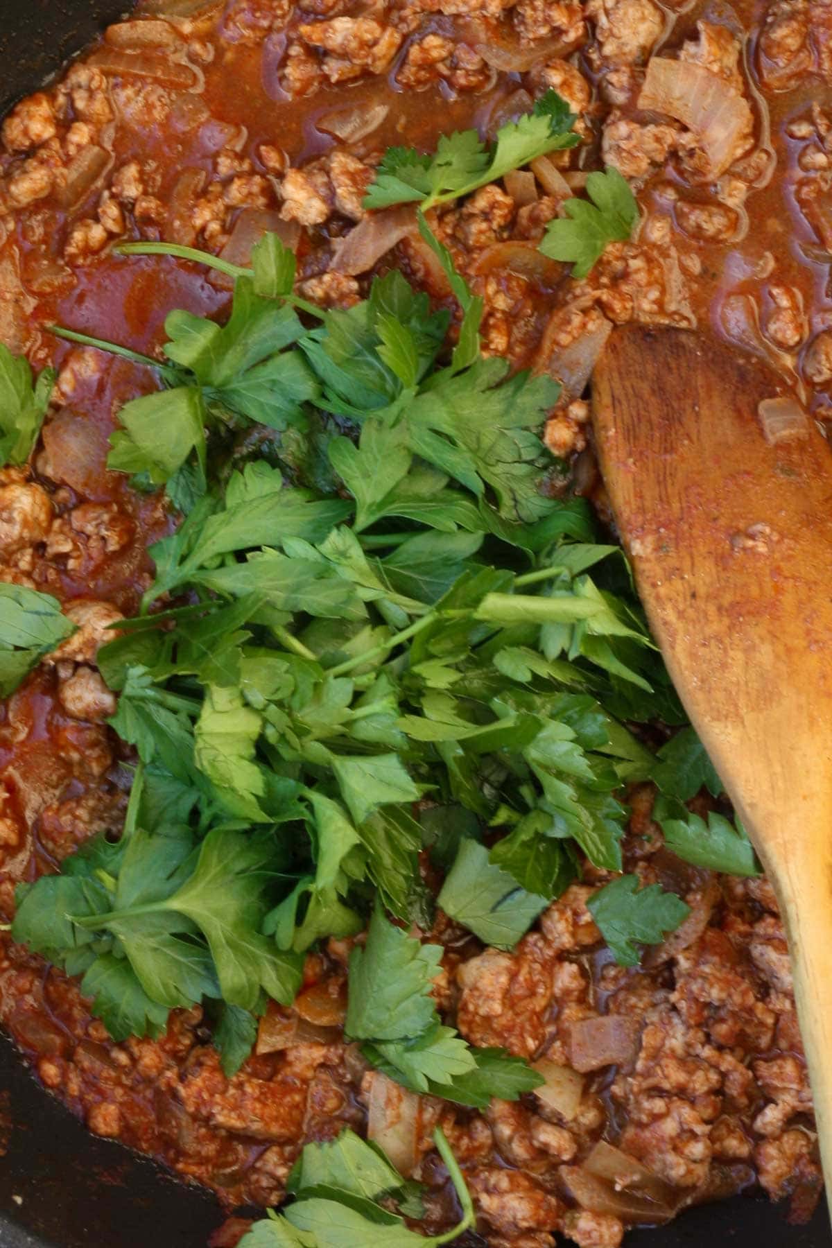 The pasta sauce with fresh parsley on top in a pan with a wooden spoon.