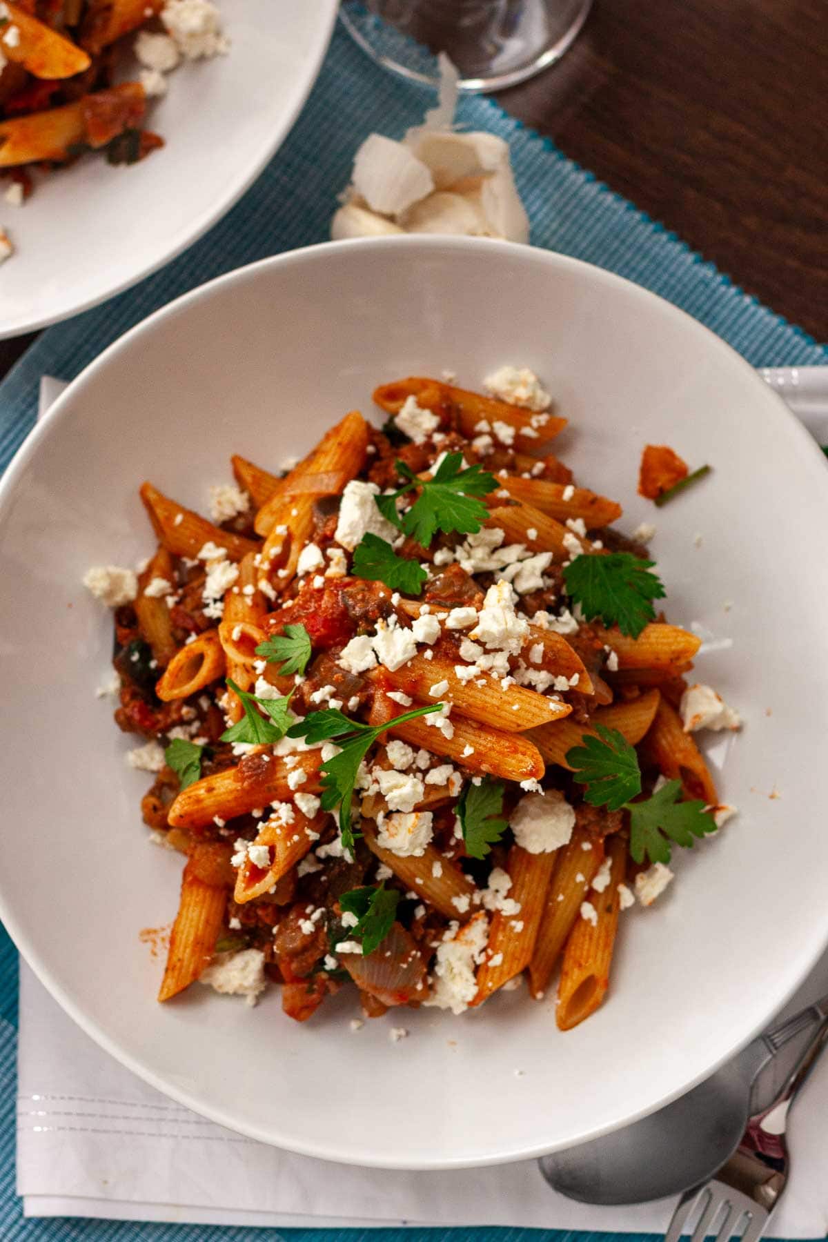 Overhead of eggplant and ground beef pasta with feta and parsley on top, in a white dish.