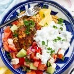 Closeup of overhead of a blue bowl of Greek chicken and rice with tomato, cucumber and feta salad and tsatziki.