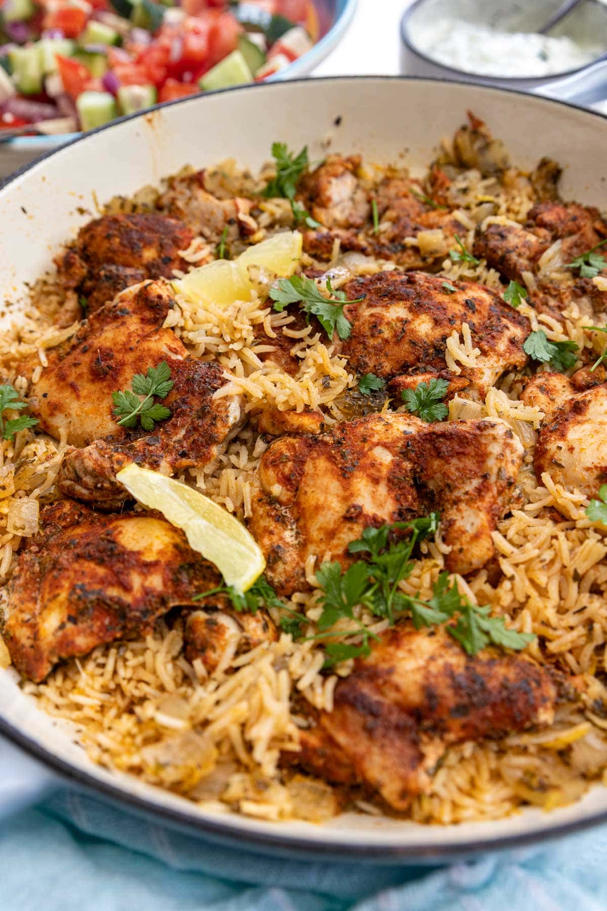 One pot Greek chicken and rice with lemon segments and parsley on top, and a light blue tea towel at the front of the pot.