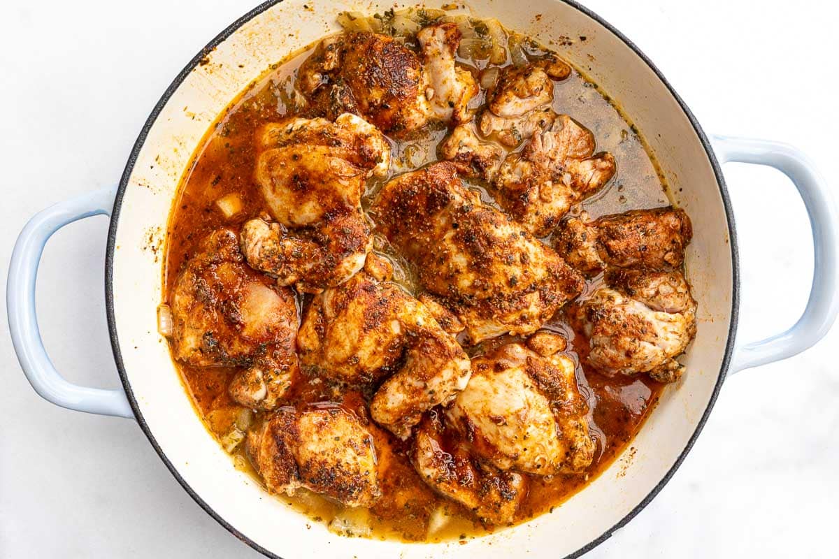 Overhead view of a pan of browned chicken thighs on top of rice and broth.