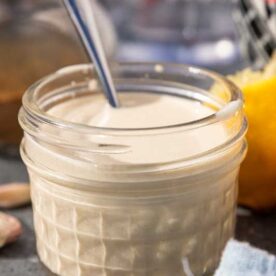 A closeup of the dressing in a small jar with a spoon in it.