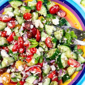 Closeup overhead of a colorful bowl of the salad, with salad servers in it.