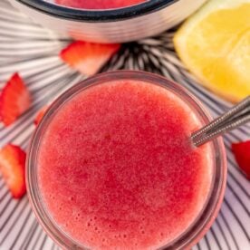 Overhead view of the puree in a small jar with a spoon in it and with ingredients and a parfait at the side.