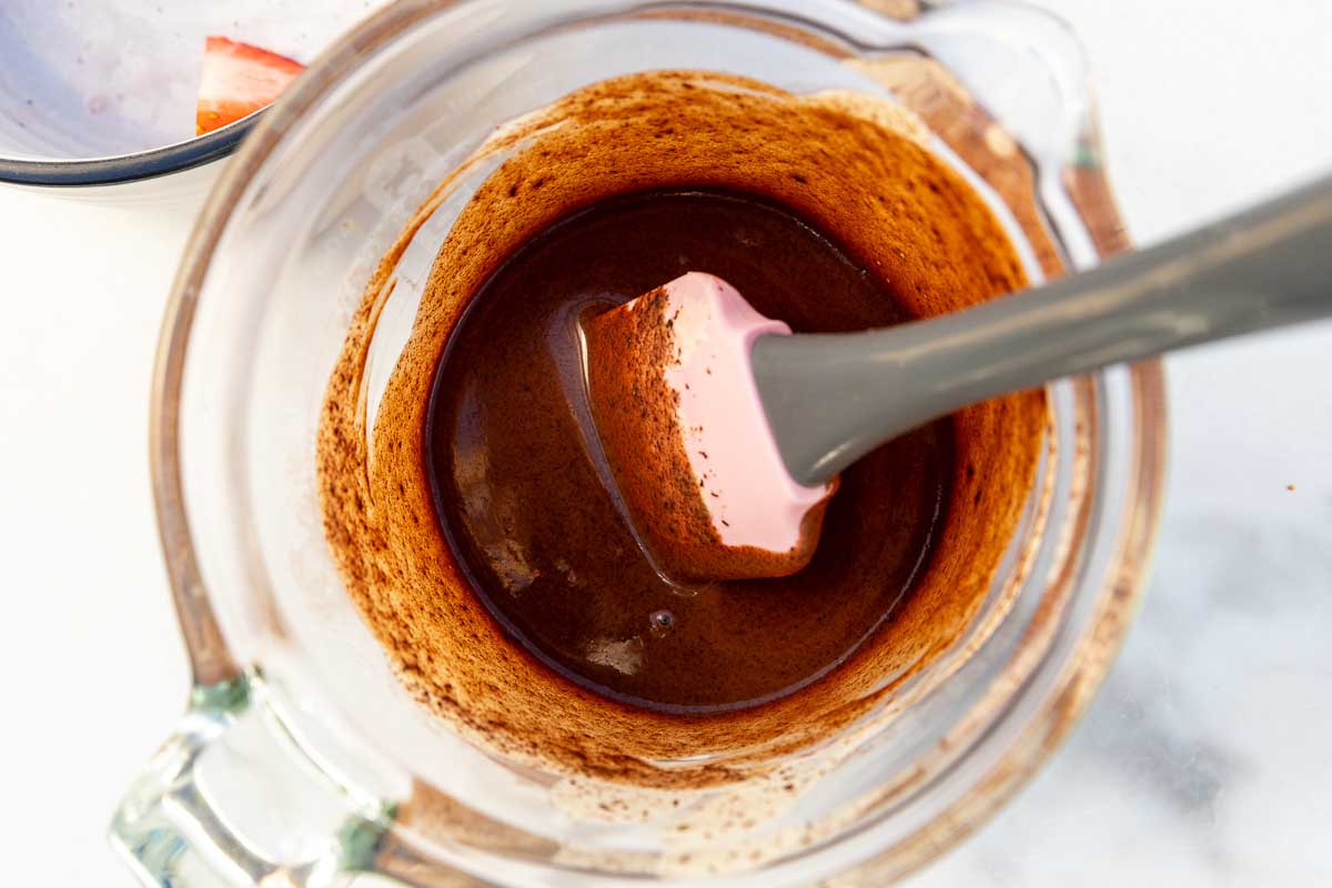 Overhead view of a jug of hot chocolate sauce mixture, with a pink spatula in it.