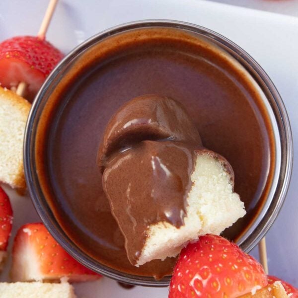 Someone dipping cake and strawberries into a small glass bowl of homemade chocolate dipping sauce.