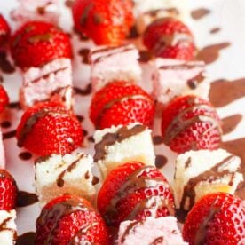 Closeup view of strawberries and angel food cake on wooden skewers with chocolate sauce drizzled all over.