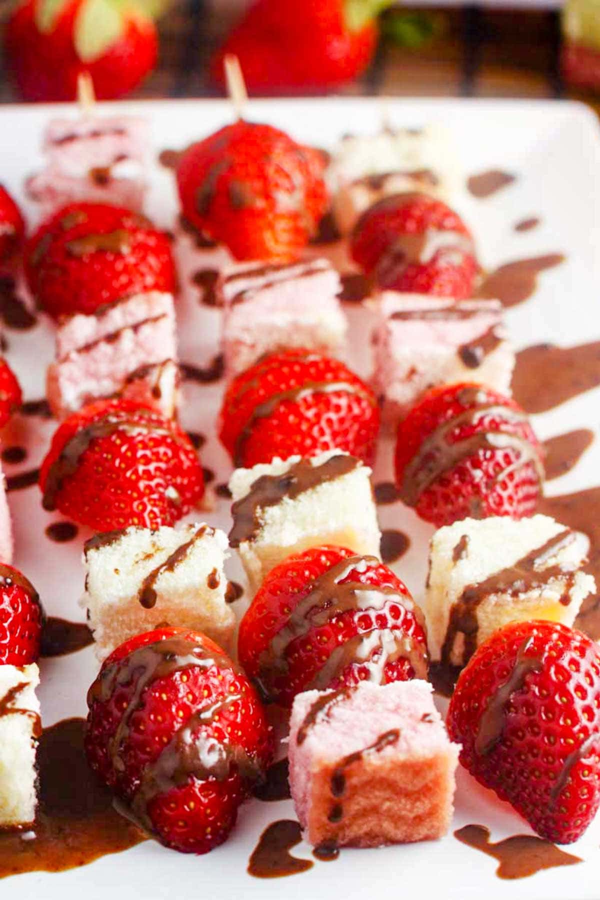 Closeup view of strawberries and angel food cake on wooden skewers with chocolate sauce drizzled all over.