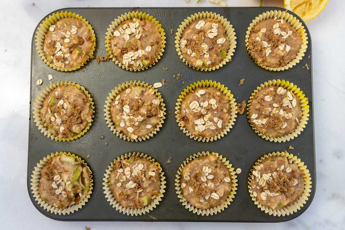 Unbaked apple oat muffins in yellow muffin cases ready to bake in a muffin pan.