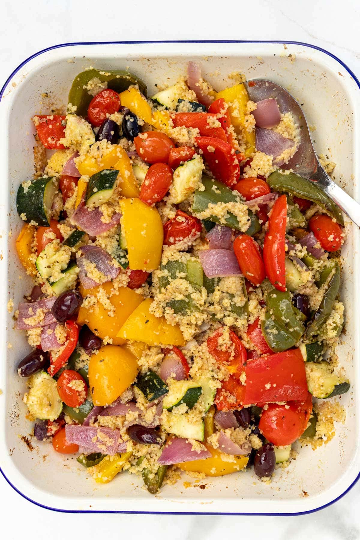 Overhead view of a baking dish of roasted vegetables and couscous, with a serving spoon in it.